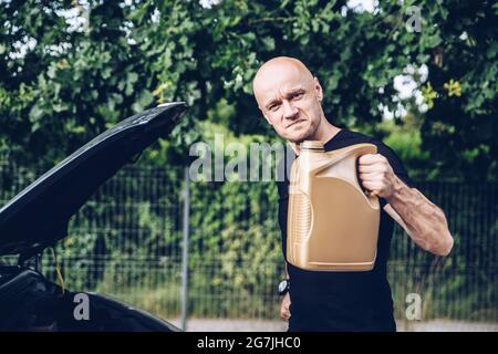 Bell'uomo in t-shirt nera con bottiglia di olio motore. Foto Stock