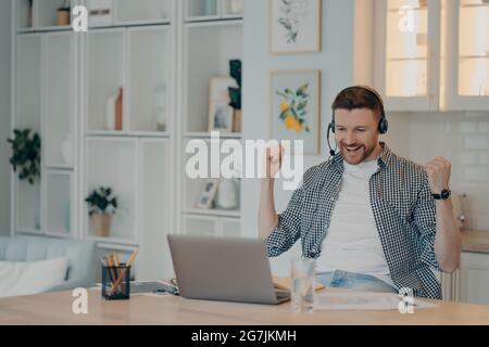 Sorridente freelance maschile che festeggia il successo e guarda lo schermo del laptop Foto Stock