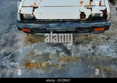 Vecchia auto abbandonata e arrugginita parcheggiata su un pavimento di cemento. Foto Stock