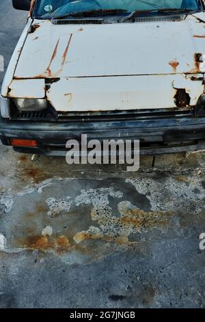 Vecchia auto abbandonata e arrugginita parcheggiata su un pavimento di cemento. Foto Stock