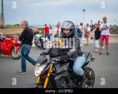 Courseulles-sur-Mer, Francia 2021 luglio. Una donna che sorride in un casco su una motocicletta con un cane che ama il motociclismo, un cane che indossa occhiali Foto Stock