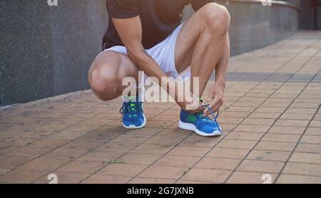 Primo piano di scarpe sportive che legano le sneaker blu mentre si preparano per l'allenamento all'aperto Foto Stock