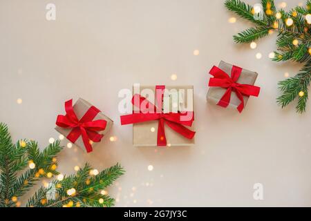 Natale e Capodanno di sfondo. Rami dell'albero di Natale, tre scatole regalo con archi rossi su sfondo beige. Vista dall'alto, disposizione piatta, spazio per la copia Foto Stock
