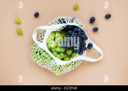 Uve fresche verdi e blu in un sacchetto a corda su sfondo beige. Zero sprechi, nessun concetto di plastica. Vista dall'alto, disposizione piatta. Foto Stock