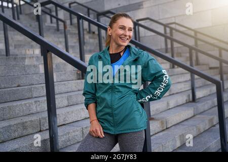 Felice sportivo di mezza età in abbigliamento sportivo sorridente in piedi fuori dopo l'allenamento mattutino in città Foto Stock