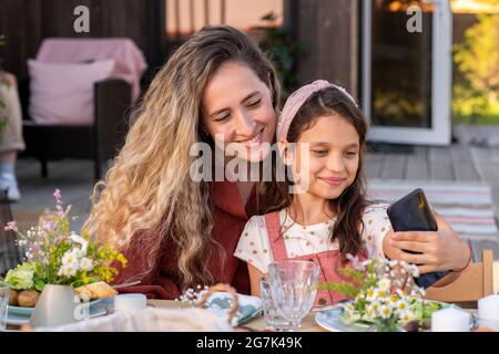 Bella giovane donna che fotografa con la sua adorabile figlia presteen a cena di famiglia Foto Stock