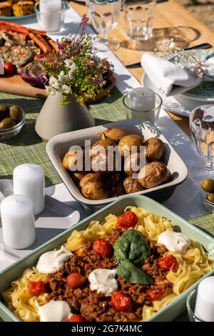 Vassoi di patate al forno e spaghetti bolognesi sul tavolo da pranzo decorato con candele e fiori Foto Stock