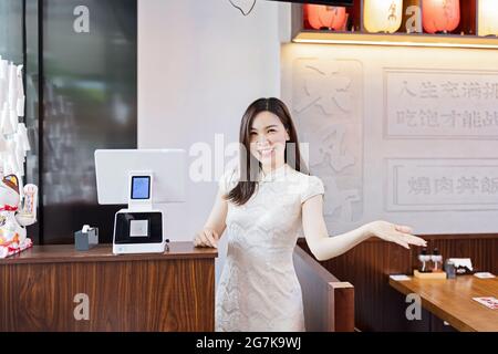 Ritratto candido di giovane donna asiatica che indossa abiti tradizionali di nome cheongsam e sorridente in caffetteria. Bancone cinese per ordinare cibo per mangiare in Foto Stock