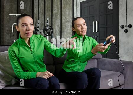 Console di gioco nelle mani di donna appassionata che si siede sul divano in appartamento loft accanto alla sorella e gioca giochi per computer. Foto Stock