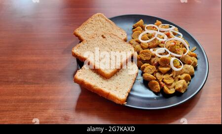 Primo piano della ricetta dei pezzi di soia con pane marrone nel piatto da portata nero su un tavolo di legno Foto Stock