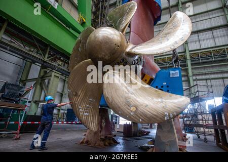 14 luglio 2021, Meclemburgo-Pomerania occidentale, Wismar: Uno dei tre Azipodi in totale è in fase di preparazione per l'installazione nel bacino del cantiere MV, accanto alla nave da crociera "Global Dream", attualmente in costruzione. Il moderno motore da 230 tonnellate con elica da 5.90 metri e motore elettrico da 19,000 kilowatt può essere ruotato di 360 gradi. La nave, destinata al mercato asiatico e che trasporta più di 5,000 passeggeri, è lunga 342 metri e alta 57 metri. La nave da crociera Global Class è fissata per diventare la più grande nave da crociera nel mondo in termini di capacità dei passeggeri. Foto Foto Stock