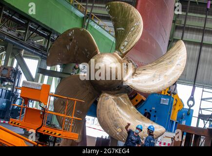 14 luglio 2021, Meclemburgo-Pomerania occidentale, Wismar: Uno dei tre Azipodi in totale è in fase di preparazione per l'installazione nel bacino del cantiere MV, accanto alla nave da crociera "Global Dream", attualmente in costruzione. Il moderno motore da 230 tonnellate con elica da 5.90 metri e motore elettrico da 19,000 kilowatt può essere ruotato di 360 gradi. La nave, destinata al mercato asiatico e che trasporta più di 5,000 passeggeri, è lunga 342 metri e alta 57 metri. La nave da crociera Global Class è fissata per diventare la più grande nave da crociera nel mondo in termini di capacità dei passeggeri. Foto Foto Stock