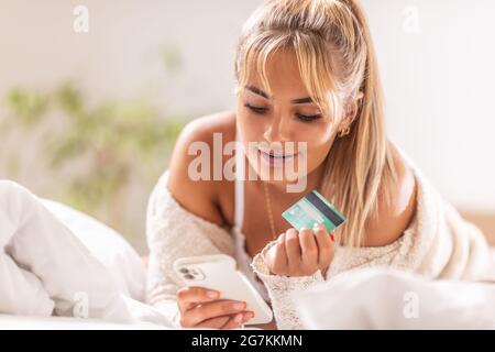 Sorridente buona-osservare la ragazza ordina roba in linea con il suo telefono delle cellule, tenendo la carta di credito in mano. Foto Stock