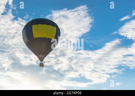 Mongolfiera e cielo blu, sole, nuvola bianca. Mongolfiera blu gialla in aria alla sera d'estate. Foto Stock