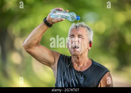 Il corridore maschio del pensionato si raffredda versando acqua fresca da una bottiglia sopra la sua testa. Foto Stock