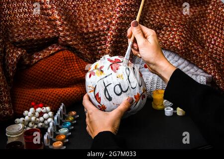 FAI DA TE. Fai da te. Donna dipinge decorazioni di ringraziamento su zucca arancione per Halloween. Vendemmia autunnale. Maglione casa accogliente. Pennello Foto Stock