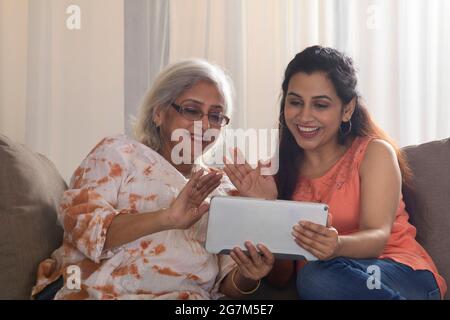 UNA DONNA ADULTA E UNA MADRE CHE PARLANO CON GLI AMICI IN VIDEOCHIAMATA SU UN TABLET Foto Stock