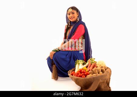 Una donna in costume Giddha seduta con un cesto di verdure al suo fianco. Foto Stock