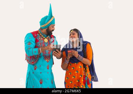 Un Bhangra e UN ballerino di Giddha che discutono giocosamente dei biils che hanno una carta di credito e del mobile in mano. Foto Stock