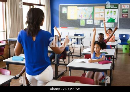 Vista posteriore di una insegnante femminile afroamericana che insegna agli studenti della classe elementare Foto Stock