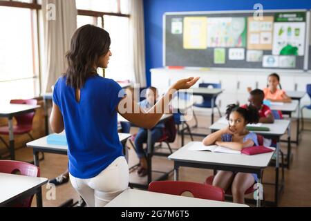 Vista posteriore di una insegnante femminile afroamericana che insegna agli studenti della classe elementare Foto Stock