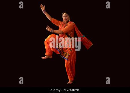 Una donna in costume di Giddha raffigurante un passo di danza con le mani e una gamba in aria. Foto Stock