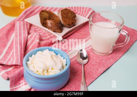 Ricotta il formaggio in una ciotola blu con panna acida e miele. Tostare il pane in un piatto. Colazione del mattino. Foto Stock