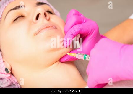 Il cosmetologist fa l'iniezione lipolitica sul mento di una giovane donna contro il doppio mento in un salone di bellezza Foto Stock