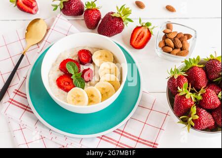 Colazione. Farinata d'avena con banane, fragole, noci sul panettino di legno. Colazione sana. Primo piano. Vista dall'alto. Foto Stock