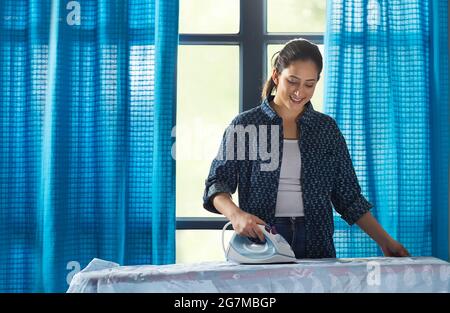 Una donna che stira i suoi vestiti in camera. Foto Stock