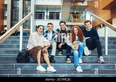 Giovani studenti sorridono mentre si siedono sulle scale dell'università. Gli studenti delle scuole superiori si siedono su passi dopo classe. Foto Stock