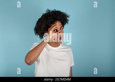 giovane uomo afro-americano che indossa una t-shirt bianca di base su uno sfondo blu pastello isolato che svanisce in shock coprendo viso e occhi con la mano, looki Foto Stock