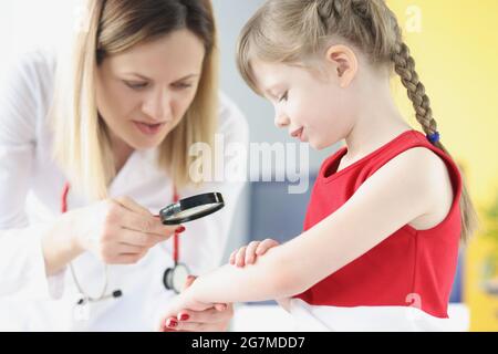 Medico pediatra esame eruzione cutanea sulla pelle di mano di bambina utilizzando lente di ingrandimento Foto Stock