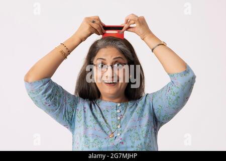 UNA DONNA ANZIANA ADULTA CHE TIENE GIOCOSAMENTE LA CARTA DI DEBITO SOPRA LA TESTA Foto Stock