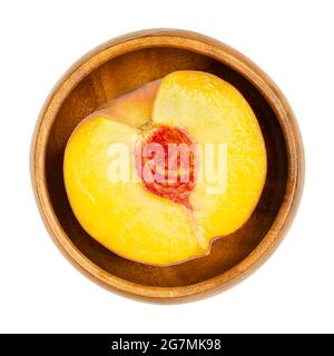 Pesche metà in una ciotola di legno. Sezione trasversale di un frutto maturo, con polpa di frutta gialla succosa, pietra arenaria rossa al centro e pelle vellutata. Foto Stock