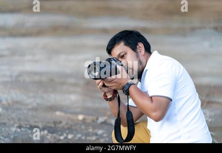Barba asiatica professionale - baffi fotocamera uomo postura e messa a fuoco in mirino e schermo LED su mirrorless fotocamera formato medio in costruzione conpr Foto Stock