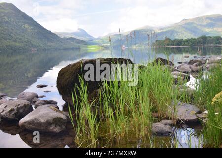 Ullswater nel distretto dei laghi catturato presto in una giornata estiva con le colline circostanti e il cielo che si riflette sulla sua superficie calma. Foto Stock