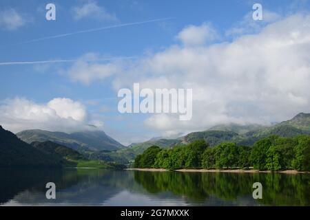 Ullswater nel distretto dei laghi catturato presto in una giornata estiva con le colline circostanti e il cielo che si riflette sulla sua superficie calma. Foto Stock