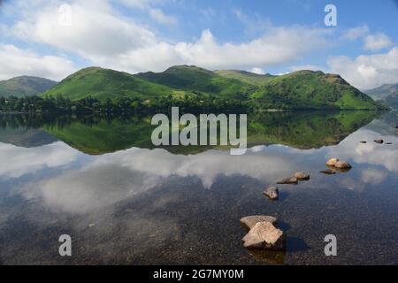 Ullswater nel distretto dei laghi catturato presto in una giornata estiva con le colline circostanti e il cielo che si riflette sulla sua superficie calma. Foto Stock