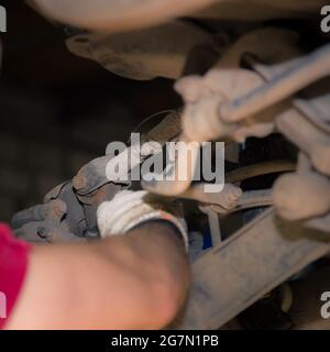 Le mani dell'uomo svitano il silent block nel telaio della vettura. Nel garage, un uomo cambia le parti di un veicolo. Concetto di piccola impresa, servizio di riparazione auto e manutenzione. 4K UHD. Foto Stock