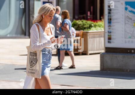 Dundee, Tayside, Scozia, Regno Unito. 15 luglio 2021. Regno Unito Meteo: Caldo sole in tutto il Nord-Est della Scozia con temperature che raggiungono i 20°C. Una giovane studentessa alla moda della St Andrews University prende la giornata per godersi il tempo estivo mentre invia messaggi sul suo i Phone nel centro di Dundee. Credit: Dundee Photographics/Alamy Live News Foto Stock