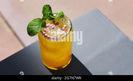 Bella limonata rinfrescante decorata con caramelle rotonde rosa e menta. Cocktail giallo con ghiaccio sul balcone. Drink estivo. Foto in formato Web Foto Stock