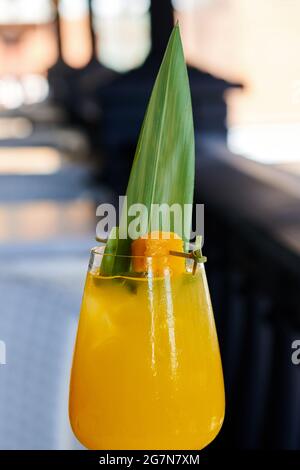 Limonata di mango gialla decorata con fettine di mango e foglia di bambù. Cocktail alcolici con ghiaccio nel ristorante. Bevanda rinfrescante in bicchiere umido. Verticale Foto Stock