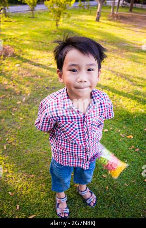 Bambino asiatico piccolo che tiene il mangime colorato del pesce, ragazzo simpatico sorridente e divertirsi nel parco il giorno d'estate, sfondo della natura. All'aperto Foto Stock
