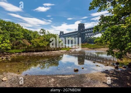 Il Ponte Britannia dalla costa dello stretto di Menai a bassa marea, Anglesey, Galles del Nord Foto Stock