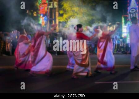 Immagine offuscata di donne indù bengalesi vestite di rosso e bianco Saris, abito tradizionale indiano, ballano con fumo santo al carnevale di Durga Puja su Foto Stock