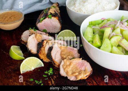 Tenderloin di maiale tailandese alla griglia con salsa di arachidi al cocco: Filetto di maiale alla griglia con salsa di arachidi, insalata di cetrioli e riso al gelsomino Foto Stock