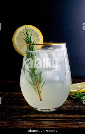 Cocktail al rosmarino Gin Fizz con Garnish: Un cocktail di gin, limone e rosmarino servito su ghiaccio e guarnito con una fetta di limone e un rametto di rosmarino Foto Stock