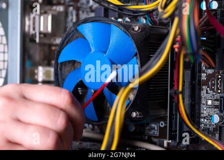 Parti interne di un vecchio personal computer. Scheda madre, scheda video e ventola polverose. Il master pulisce il radiatore del PC dalla polvere. PC rotto Foto Stock