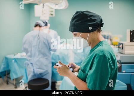 Infermiera femminile che usa il telefono cellulare all'interno della sala operatoria dell'ospedale moderno - Focus sul viso della donna Foto Stock